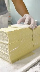 using a handheld metal knife to cut many thin layers of yellow dough into several square pieces