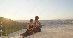 Mindful peaceful diverse women with a calm look chatting with each other and meditates outdoors, while sitting at the yoga mat. Females trying to relax after long hours of working