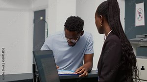 African american patient filling in medical report papers at hospital reception desk, talking to receptionist about consultation appointment. Employee giving assistance to man writing checkup form.