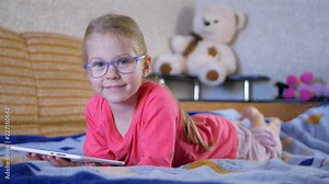 Beautiful child little girl playing with a tablet PC while lying on the sofa