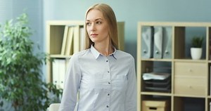 Portrait of the beautiful young woman standing in front of the camera in the office room, crossing her hands and posing.