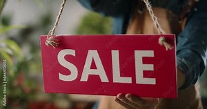 Flower shop employee hanging sale wooden sign on glass entrance door. Employee or shop owner putting announcement sign - entrepreneurship, small business 4k footage