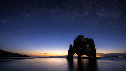 A natural stone arch beneath a sky filled with a million stars