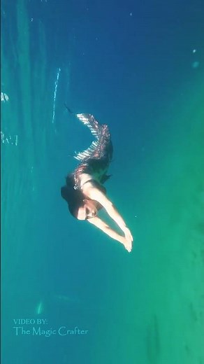 A red mermaid glides through clear blue water 🩵