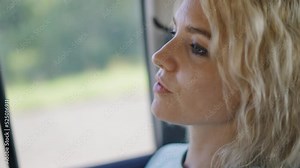 A beautiful blonde is riding in a car in the back seat. She smiles and is a little embarrassed. Slow motion.