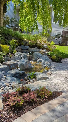 This peaceful backyard escape brings nature right to the edge of the patio. A gentle stream flows alongside where you sit, framed by lush plants and a graceful weeping willow. It feels like a little slice of nature has been tucked right into the backyard — a calm, soothing space to relax, listen, and unwind. 🌿💧 #fontanapondsandwaterfeatures #pondlesswaterfall #landscapedesign #waterfeature #livethefontanalifestyle #outdoorliving #backyardwaterfall #peaceful | Fontana Ponds & Water Features