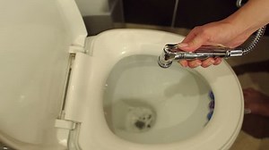 Young woman using a bidet shower in the toilet, close-up. Modern design home bidet spray cleaning flush toilet in bathroom.
