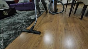 Professional office cleaner using vacuum cleaner to clean carpet around desk and chair in modern office with bookshelf or personal library in the background, ensuring clean and tidy office environment Stock Video