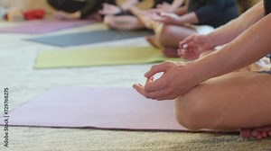 Low section of women meditating while sitting on mat. Females are practicing yoga in healthcare studio. They are relaxing together at club.
