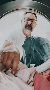 Man filling an automatic washing machine inside a laundromat while a woman stands in the background, seen from inside the drum. Concept of household chores and laundry while traveling